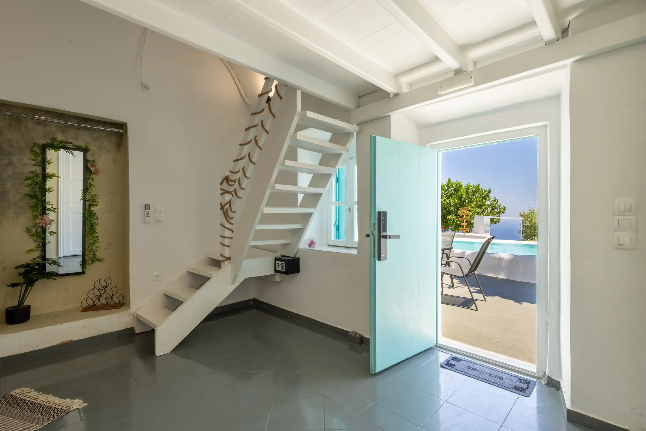Athiri suite — entrance hall with a white staircase and an open turquoise door onto the sea-view terrace