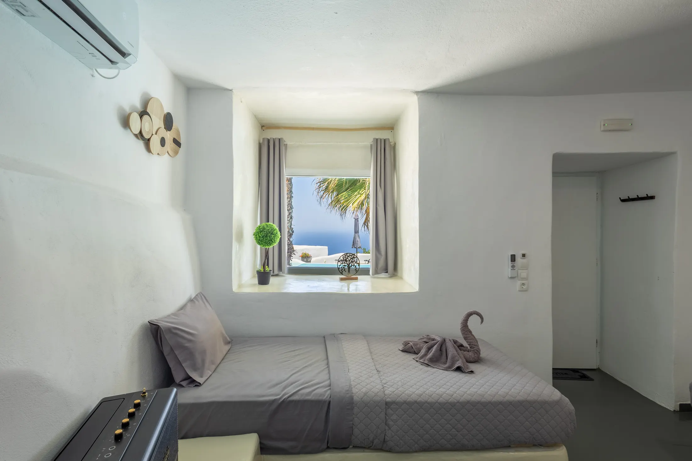 Voutyra suite — bedroom with a bed set in an alcove beneath a deep-set window looking out to the sea